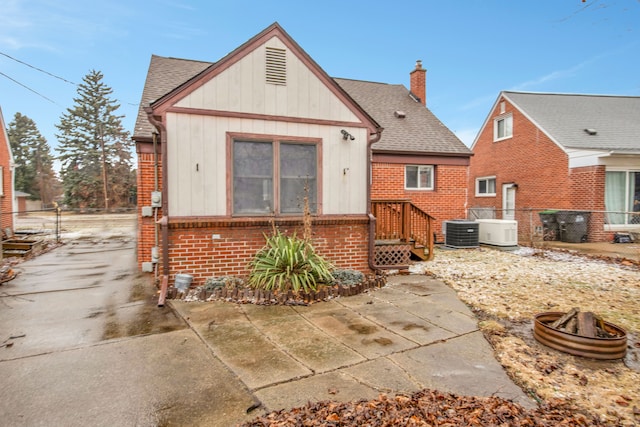 rear view of property featuring central AC, brick siding, a chimney, and a shingled roof