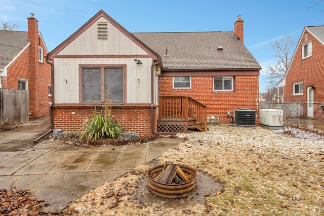 rear view of property featuring an outdoor fire pit, a shingled roof, fence, central AC, and brick siding