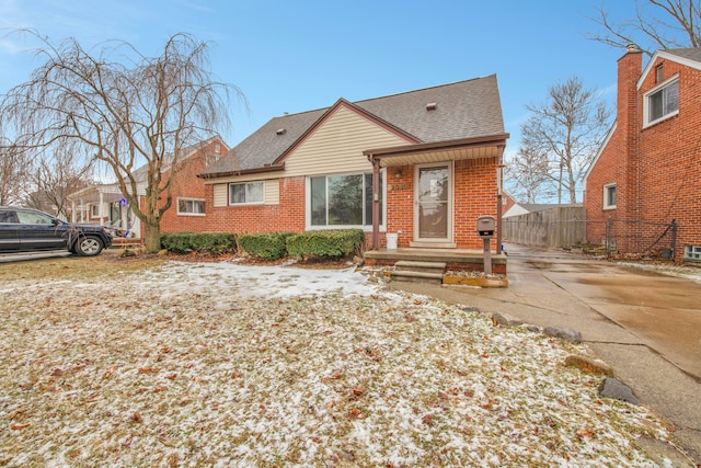 view of front of home with a shingled roof, brick siding, and fence