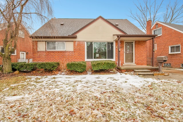 snow covered rear of property featuring roof with shingles and brick siding