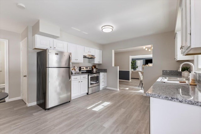 kitchen with appliances with stainless steel finishes, under cabinet range hood, light wood-style floors, white cabinetry, and a sink