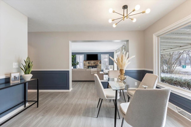 dining room with a notable chandelier, wainscoting, plenty of natural light, and light wood-style floors