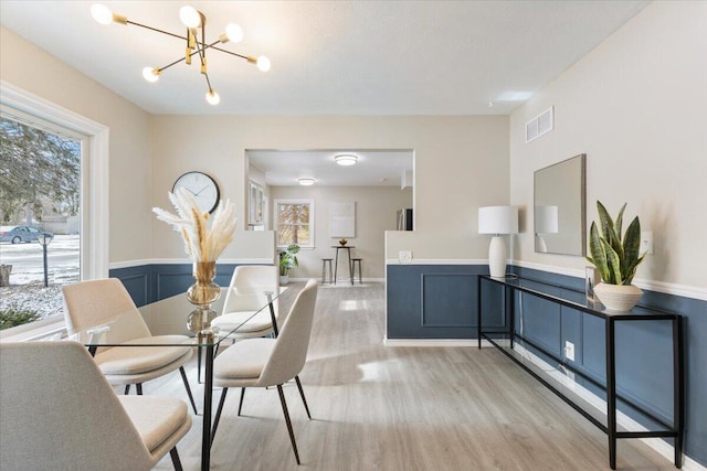 dining room featuring light wood finished floors, visible vents, a wainscoted wall, an inviting chandelier, and a decorative wall