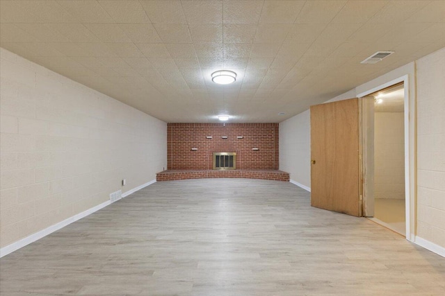 finished basement with a brick fireplace, wood finished floors, visible vents, and baseboards