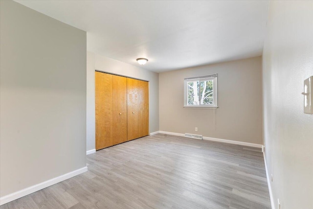 unfurnished bedroom featuring light wood-style flooring, a closet, visible vents, and baseboards