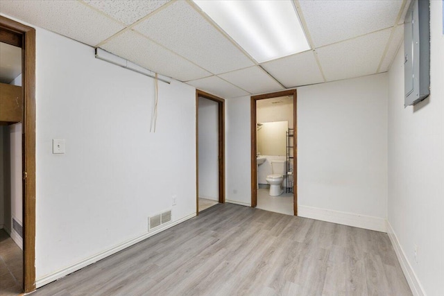 interior space with visible vents, a drop ceiling, light wood-style floors, electric panel, and baseboards