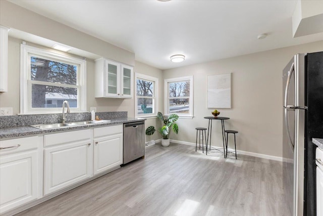 kitchen with appliances with stainless steel finishes, white cabinetry, a sink, light wood-type flooring, and baseboards