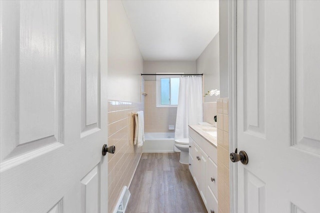 bathroom with visible vents, toilet, wood finished floors, shower / bath combo with shower curtain, and tile walls