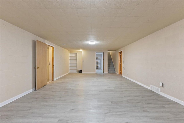 empty room with concrete block wall, wood finished floors, visible vents, and stairs