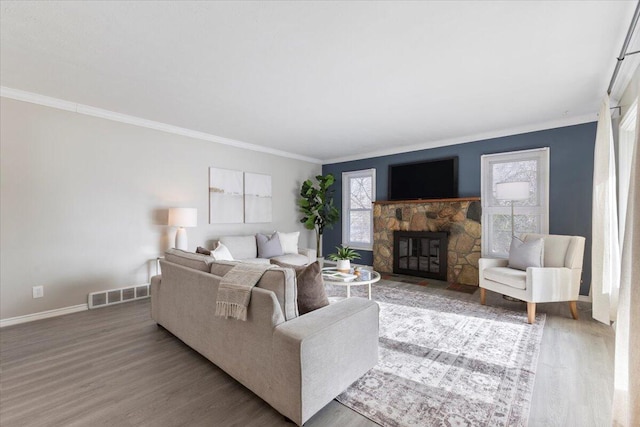 living area featuring crown molding, visible vents, a stone fireplace, wood finished floors, and baseboards