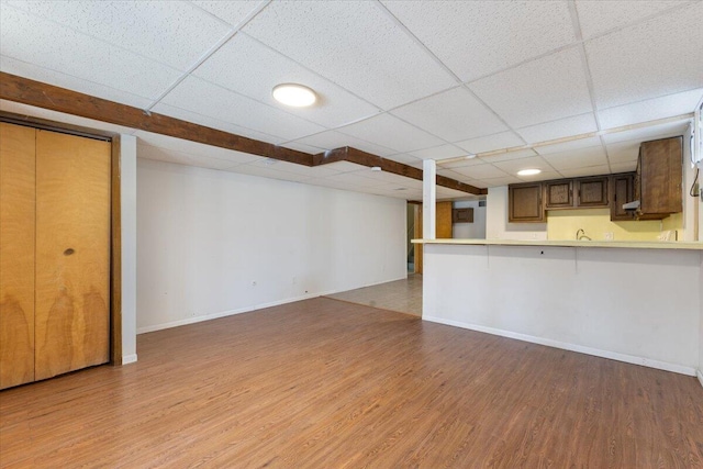 unfurnished living room featuring a paneled ceiling, baseboards, and light wood finished floors