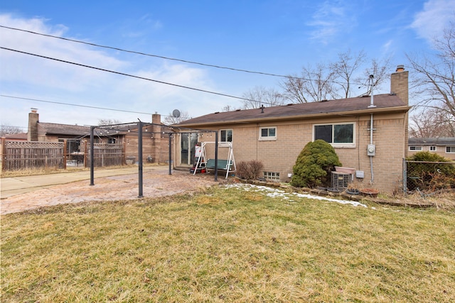 back of house featuring brick siding, a chimney, a lawn, central AC unit, and fence