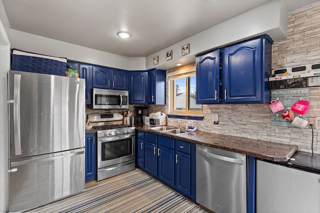 kitchen featuring appliances with stainless steel finishes, dark countertops, a sink, and blue cabinets