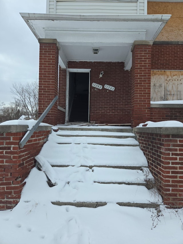 snow covered property entrance featuring brick siding