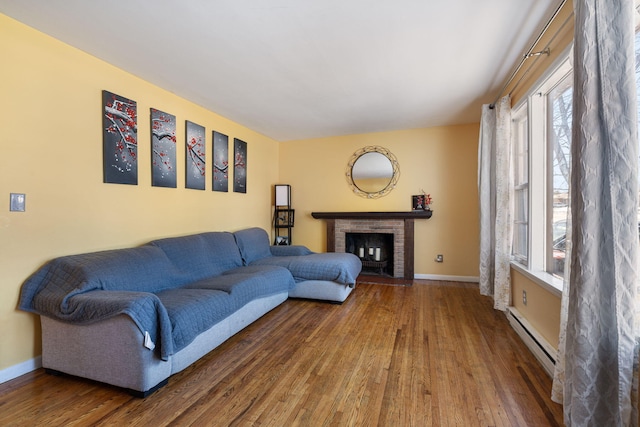 living area featuring a brick fireplace, a baseboard radiator, baseboards, and wood finished floors