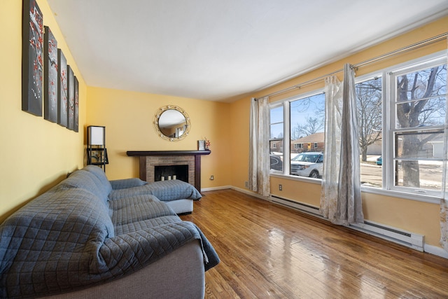 living room with a baseboard heating unit, a fireplace, baseboards, and wood finished floors