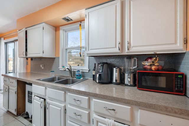 kitchen with light tile patterned floors, a sink, white cabinetry, and a healthy amount of sunlight