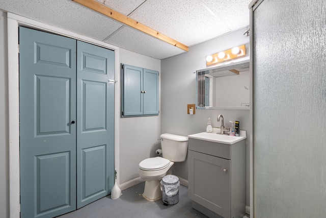 bathroom featuring a drop ceiling, toilet, concrete floors, vanity, and baseboards