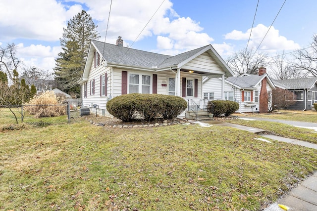 bungalow-style home with a shingled roof, a front yard, fence, and a chimney