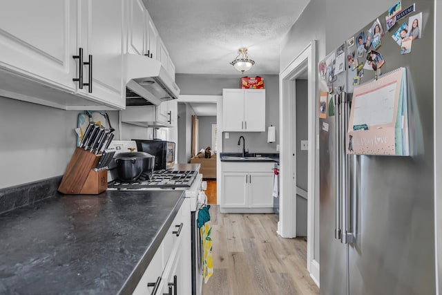 kitchen with high end fridge, gas range oven, under cabinet range hood, white cabinetry, and a sink