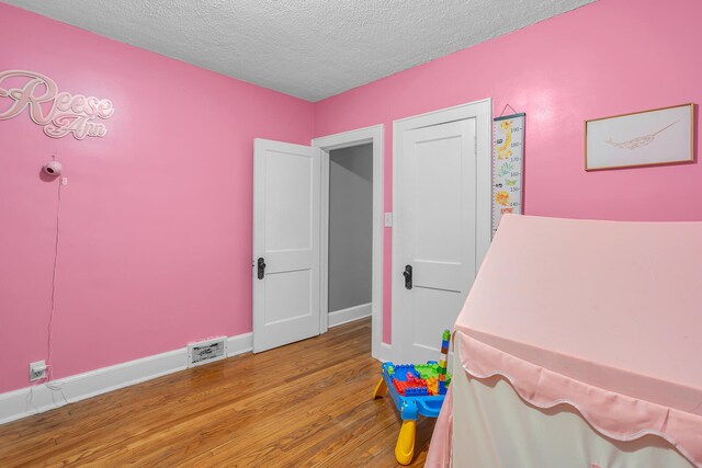 bedroom with visible vents, a textured ceiling, baseboards, and wood finished floors