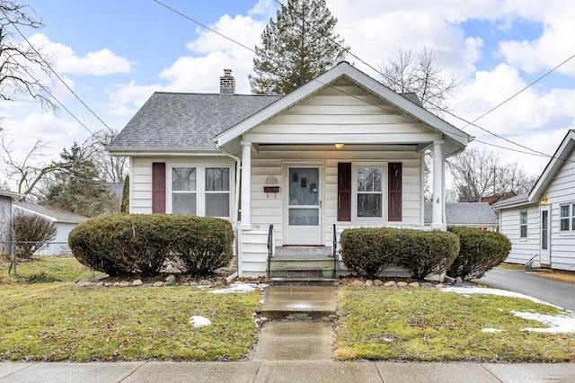 bungalow-style home featuring a front lawn, roof with shingles, a chimney, and fence