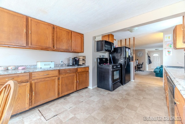 kitchen featuring black appliances, light stone counters, brown cabinetry, and a textured ceiling