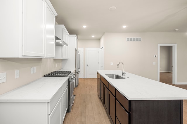 kitchen featuring a sink, white cabinets, wall chimney range hood, high end range, and a center island with sink