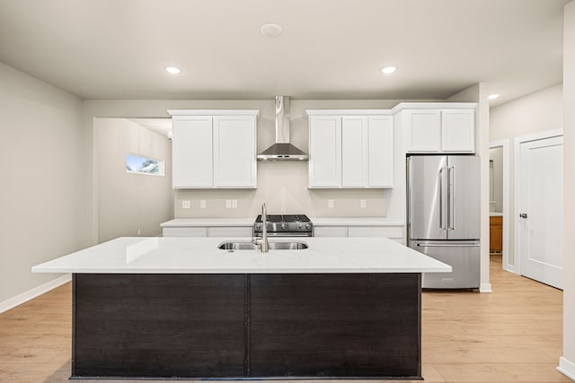 kitchen with stainless steel appliances, light wood-style floors, a sink, and wall chimney range hood