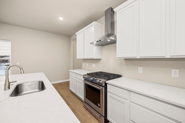 kitchen featuring a sink, white cabinets, light wood-style floors, wall chimney range hood, and high end range