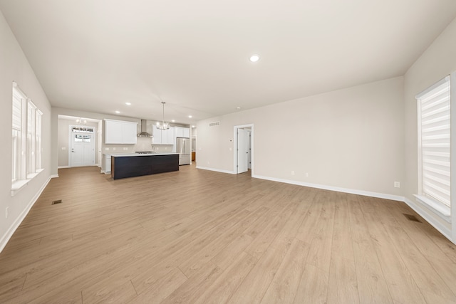 unfurnished living room featuring light wood-style floors, plenty of natural light, visible vents, and baseboards