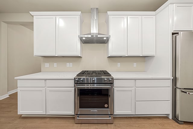 kitchen featuring appliances with stainless steel finishes, white cabinets, light stone countertops, light wood-type flooring, and wall chimney exhaust hood