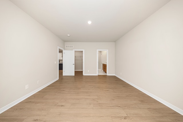 unfurnished bedroom featuring light wood-style floors, a walk in closet, visible vents, and baseboards