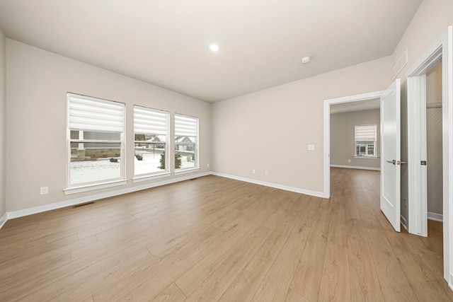 spare room with a healthy amount of sunlight, light wood finished floors, visible vents, and baseboards