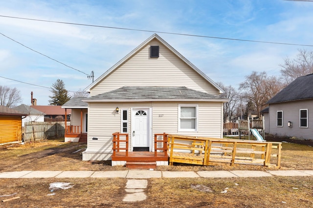 view of front of property with a shingled roof, a playground, fence, and a deck