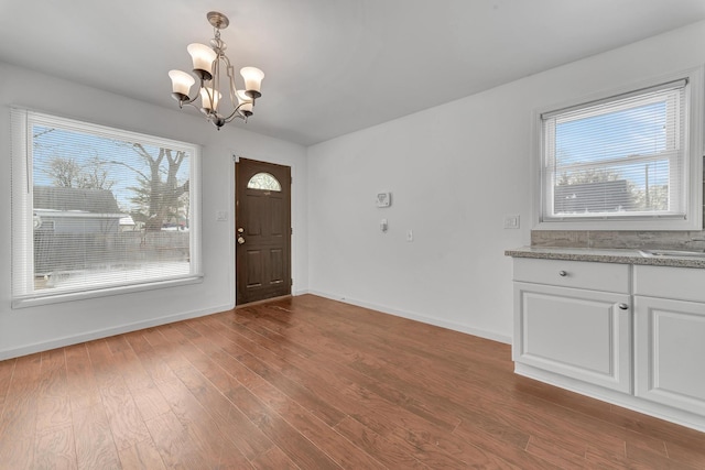 foyer entrance with dark wood-style floors, plenty of natural light, baseboards, and an inviting chandelier