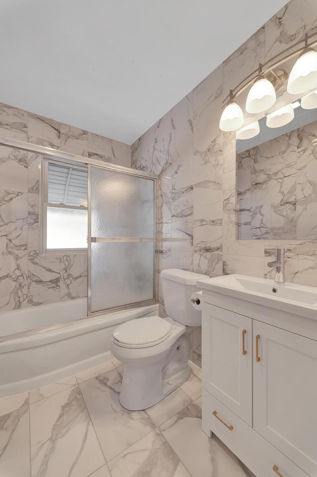 full bathroom featuring bath / shower combo with glass door, toilet, marble finish floor, vanity, and tile walls