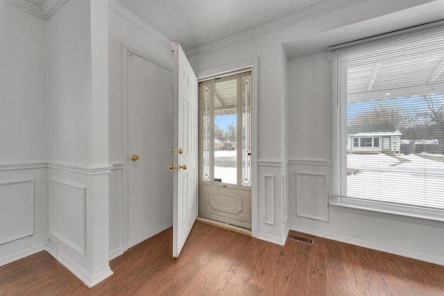 foyer featuring visible vents, wainscoting, ornamental molding, wood finished floors, and a decorative wall