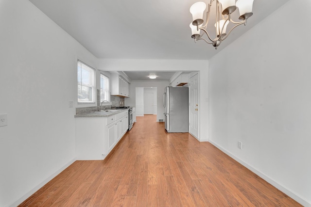 kitchen with white cabinets, appliances with stainless steel finishes, an inviting chandelier, light wood-type flooring, and backsplash