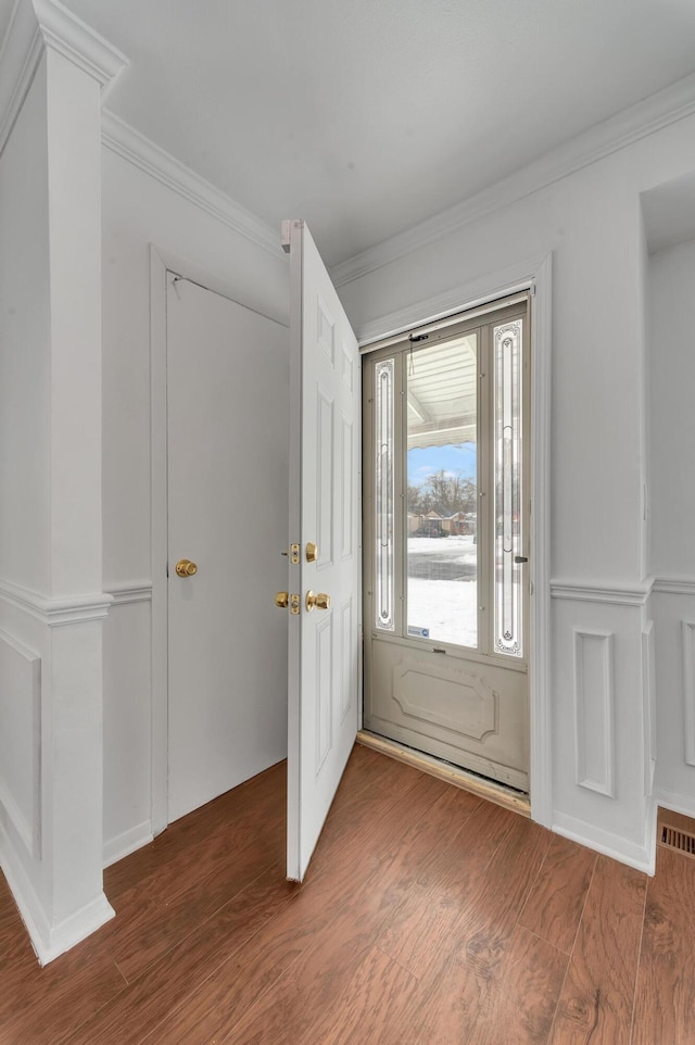 entryway featuring visible vents, crown molding, a decorative wall, and wood finished floors