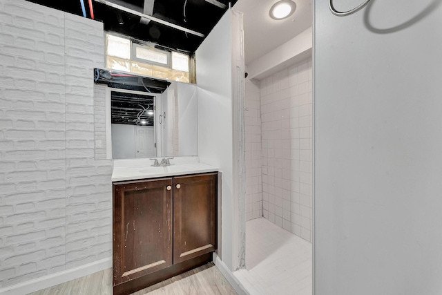 bathroom featuring tiled shower, vanity, baseboards, and wood finished floors