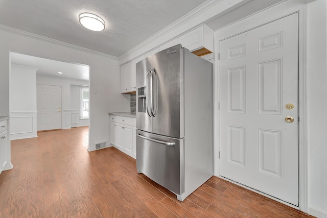 kitchen featuring stainless steel refrigerator with ice dispenser, wood finished floors, visible vents, and white cabinets