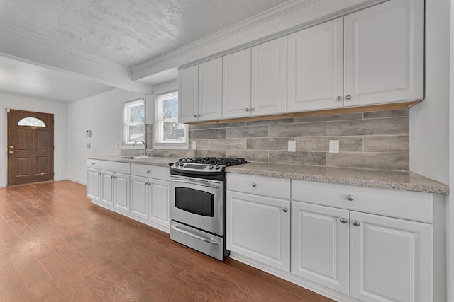 kitchen with stainless steel gas range oven, wood finished floors, a sink, white cabinets, and decorative backsplash