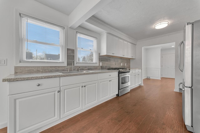 kitchen with dark wood finished floors, stainless steel appliances, crown molding, white cabinetry, and a sink