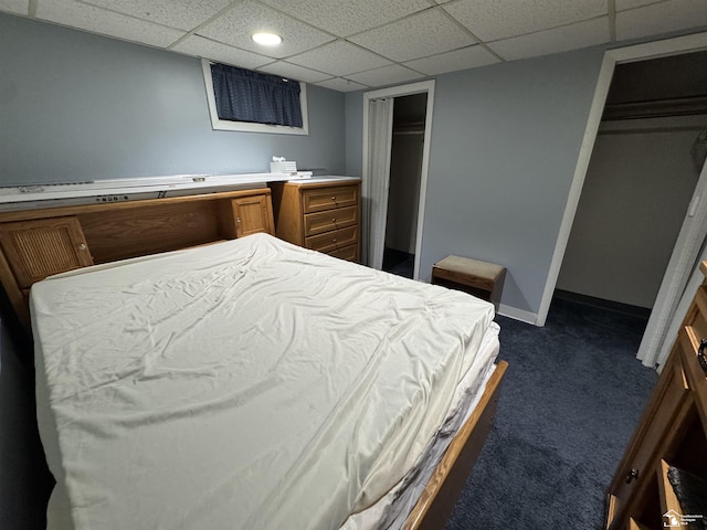 bedroom featuring a paneled ceiling, baseboards, dark colored carpet, and two closets