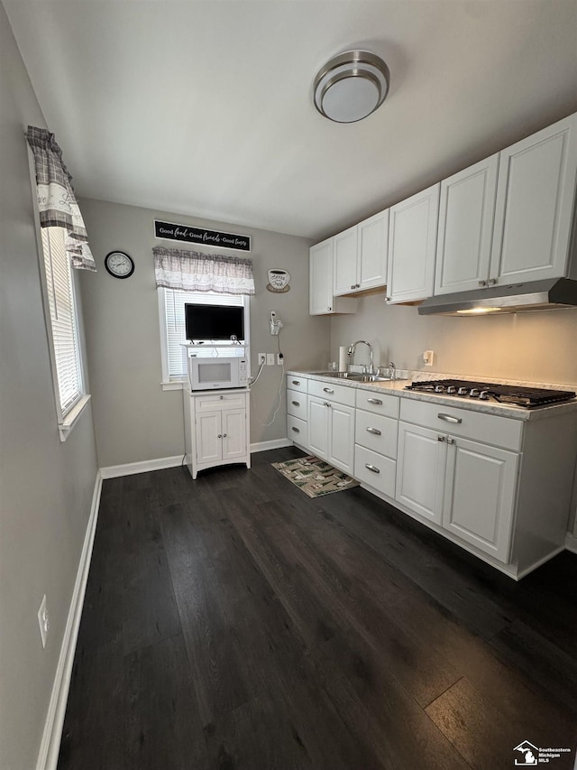 kitchen featuring white cabinets, dark wood-type flooring, under cabinet range hood, stainless steel gas cooktop, and a sink