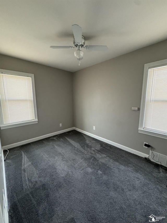 spare room with ceiling fan, dark colored carpet, visible vents, and baseboards