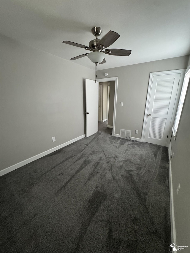 unfurnished bedroom with visible vents, baseboards, a ceiling fan, dark carpet, and a closet