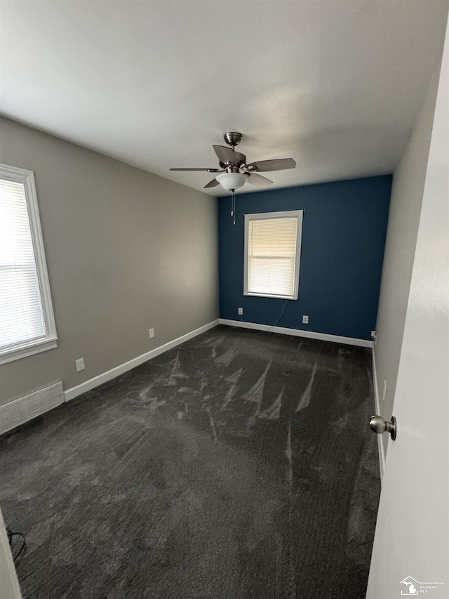 spare room with a ceiling fan, dark carpet, and baseboards