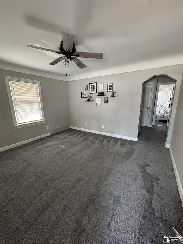 empty room with arched walkways, dark colored carpet, visible vents, and baseboards